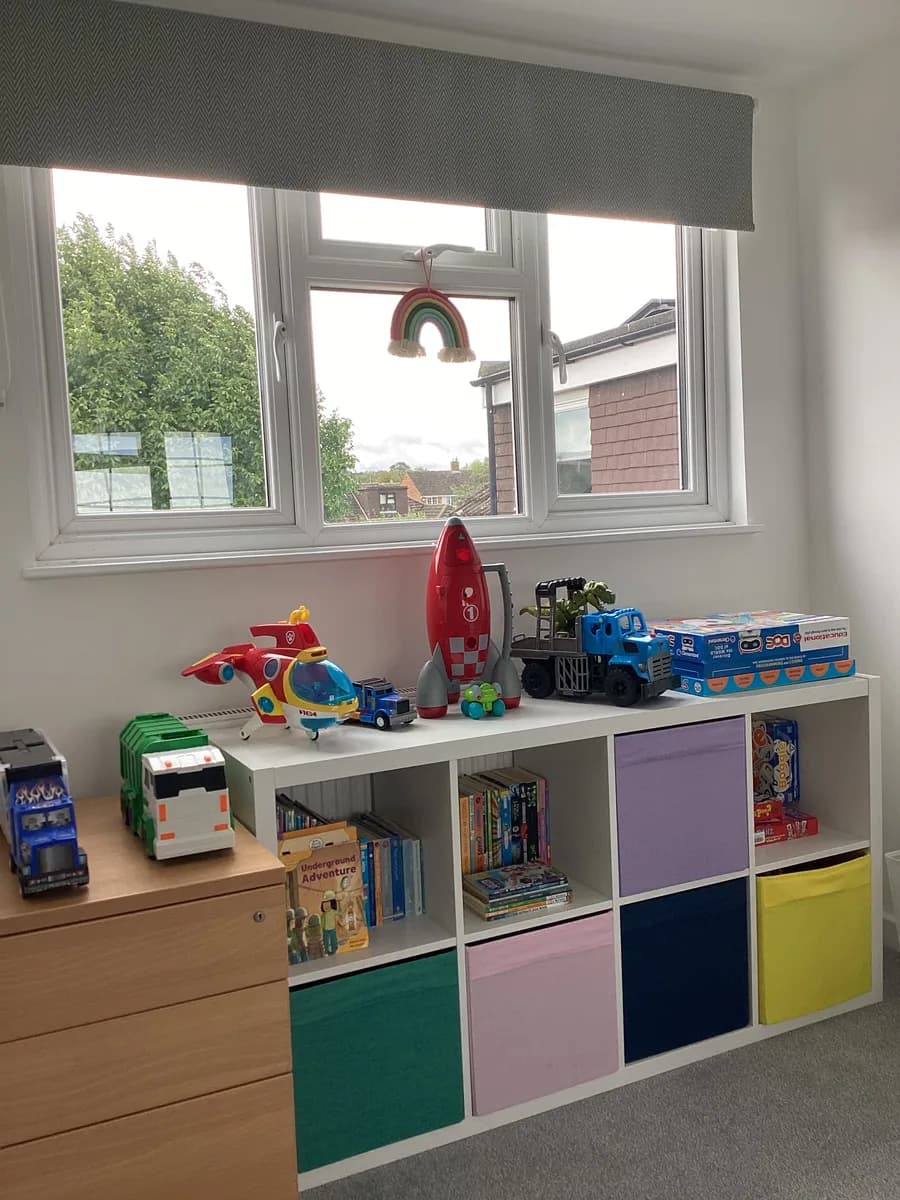Books, toy vehicles and colourful storage boxes on shelves beneath a window
