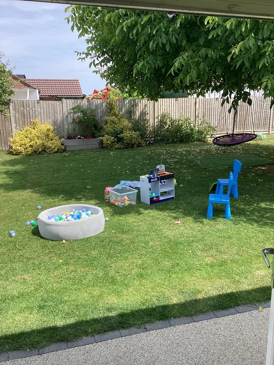 A ball pit, toy stations and blue chair set out on the lawn beneath a tree