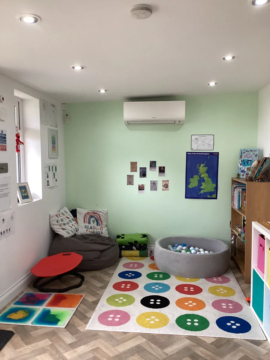 A learning room with a colourful rug, ball pit, beanbag and bookshelves