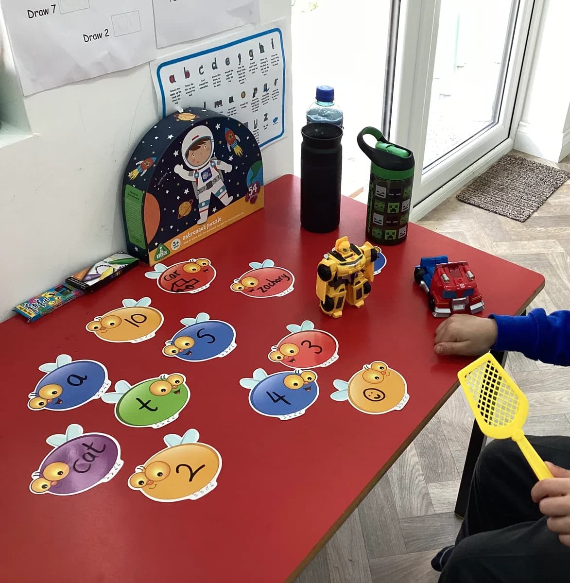 Numbered insect cards and a fly swatter on a red table for a counting game