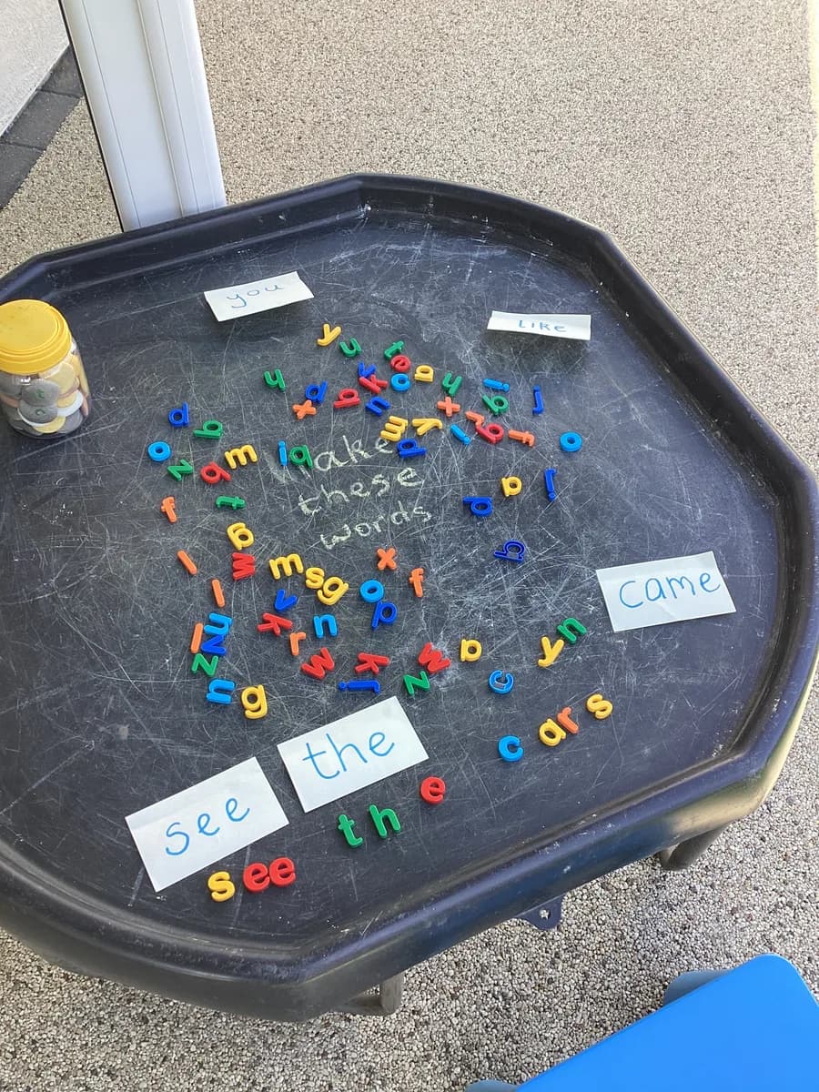 Colourful letters and word cards arranged on an activity tray outside